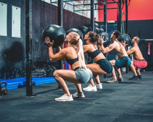 Group of sporty people doing squats with fitness ball in the gym.